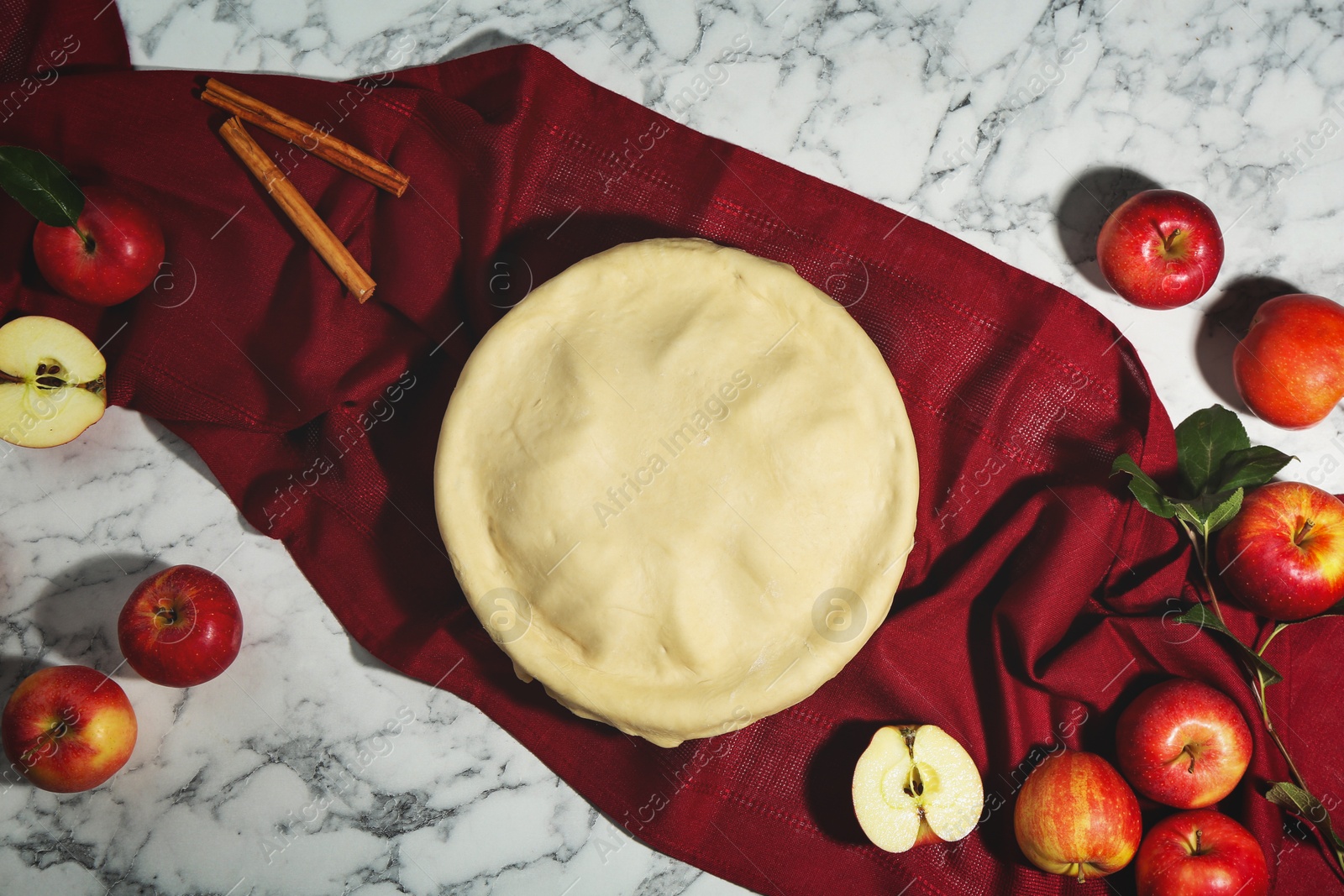 Photo of Raw homemade pie, apples and cinnamon sticks on white marble table, flat lay