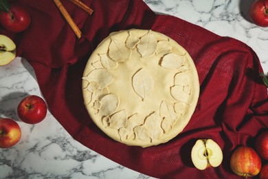 Photo of Raw homemade pie, apples and cinnamon sticks on white marble table, flat lay