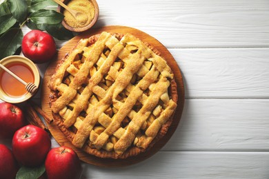 Photo of Tasty homemade apple pie and ingredients on white wooden table, flat lay. Space for text