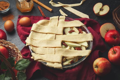 Photo of Raw homemade apple pie and ingredients on dark textured table