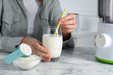 Photo of Woman with glass of protein cocktail at white marble table, closeup