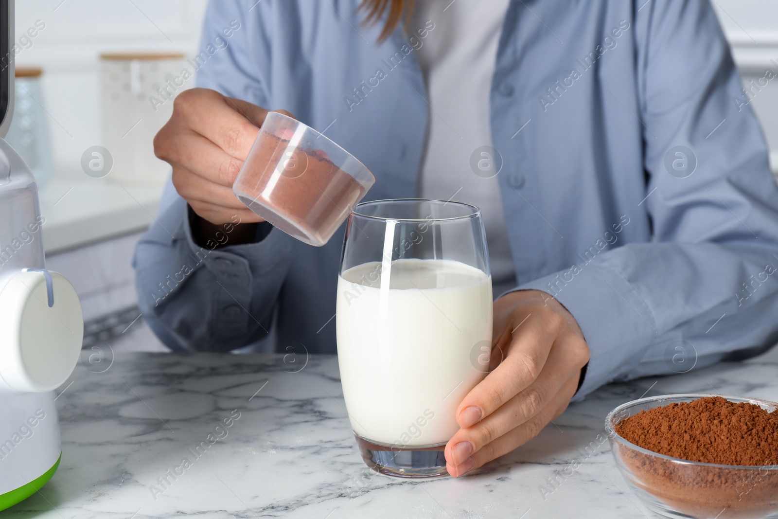 Photo of Making protein cocktail. Woman adding powder into glass with milk at white marble table, closeup