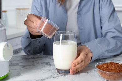 Photo of Making protein cocktail. Woman adding powder into glass with milk at white marble table, closeup