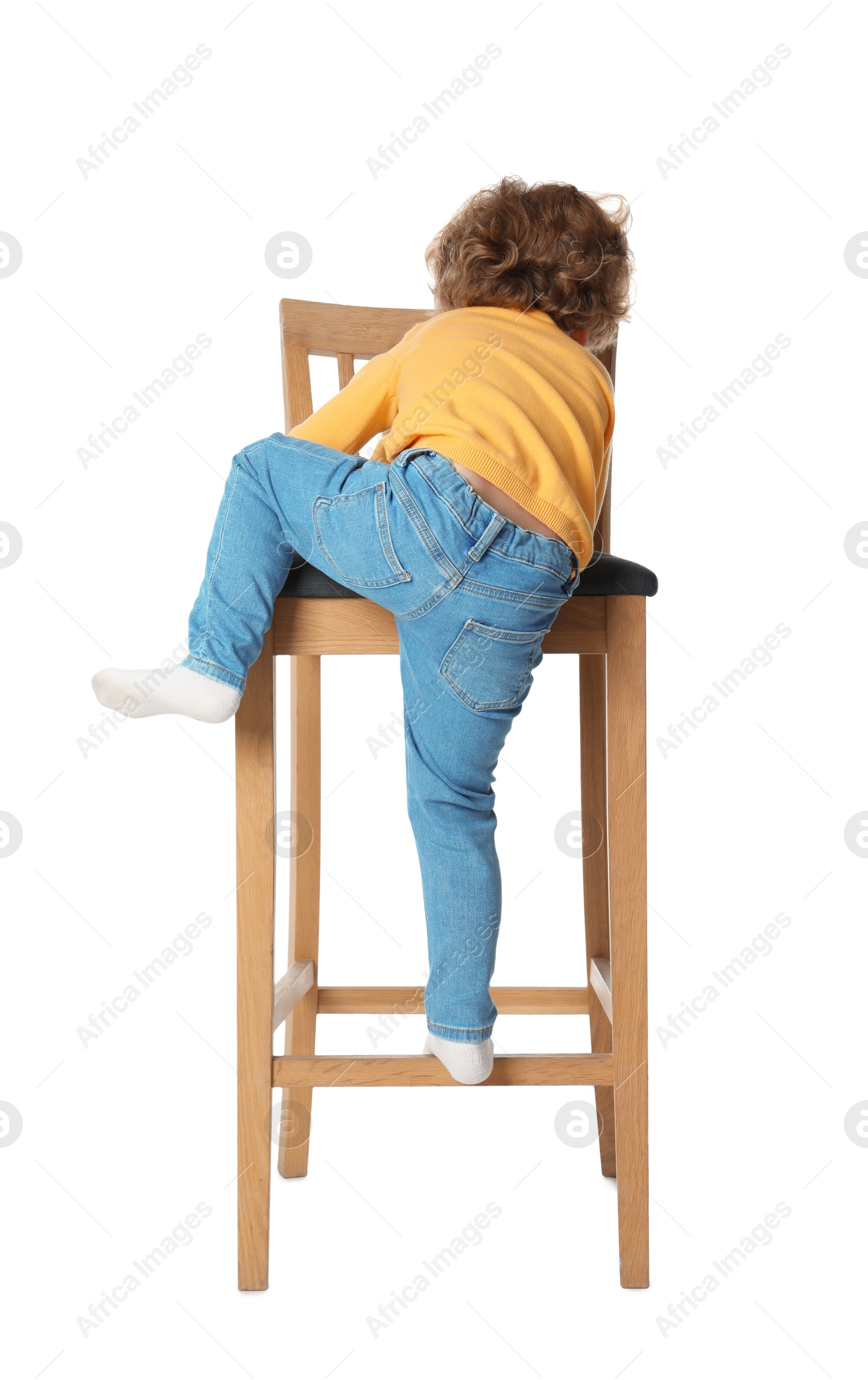 Photo of Little boy standing on stool against white background, back view