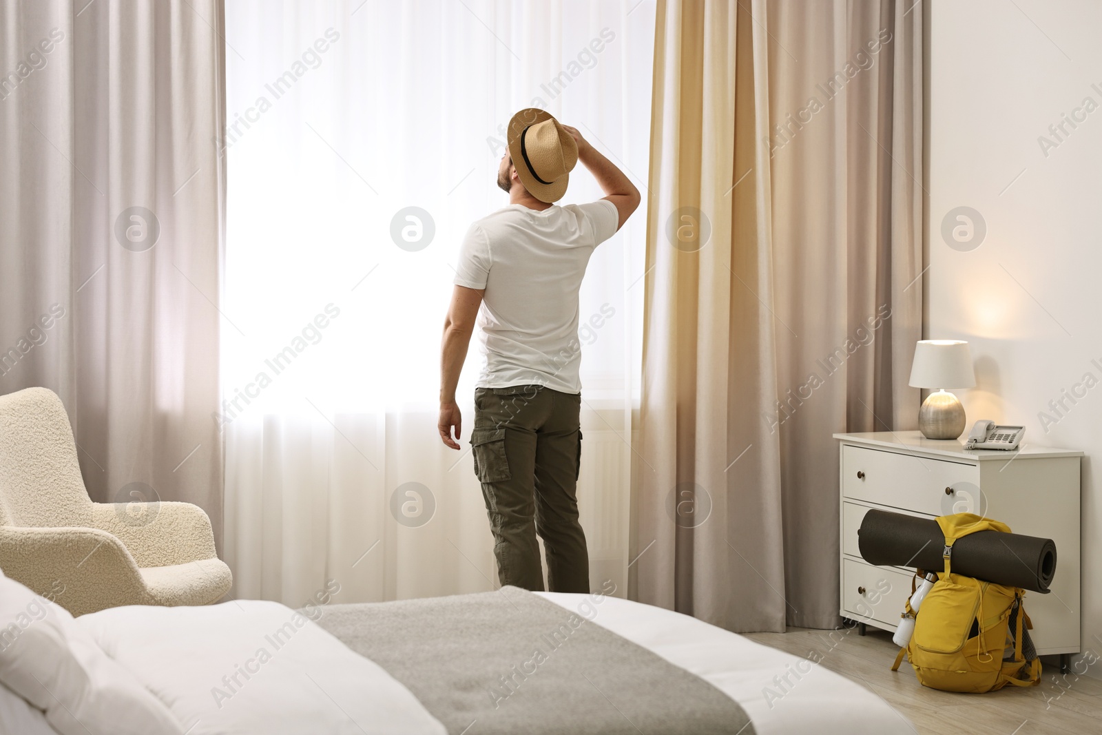 Photo of Traveller with straw hat near window in hotel room