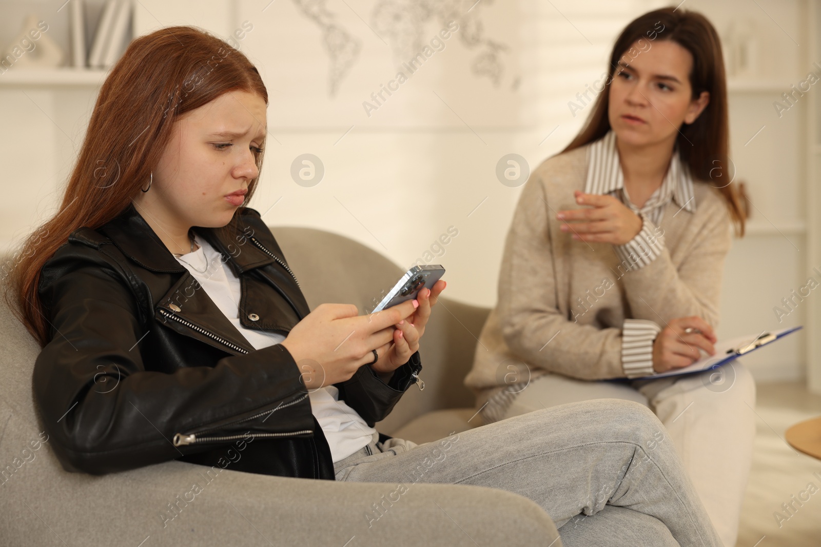 Photo of Rebellious teenage girl using smartphone instead of consultation with psychologist in office, selective focus