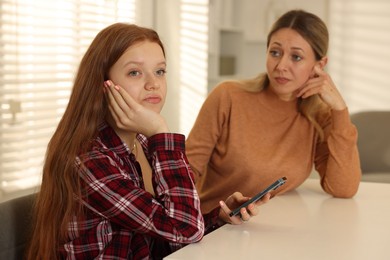 Annoyed teenage girl with smartphone and her mother at psychologist's office, selective focus