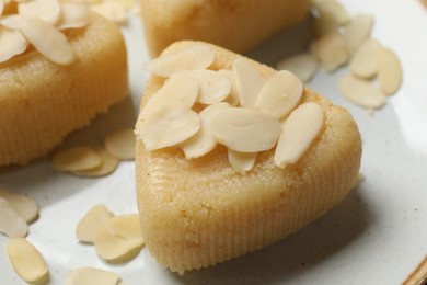 Photo of Pieces of delicious semolina halva with almond flakes on plate, closeup