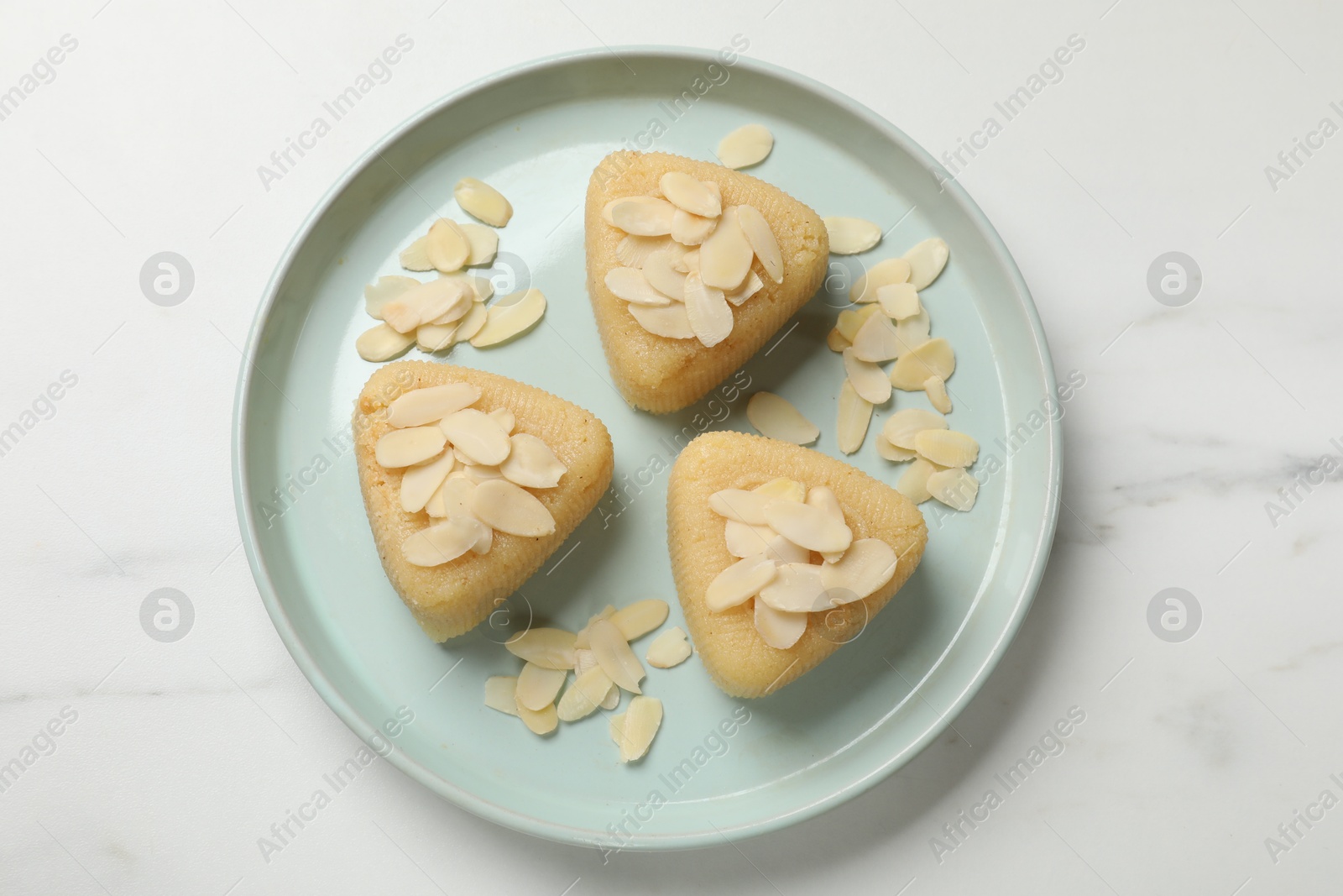 Photo of Pieces of delicious semolina halva with almond flakes on white marble table, top view