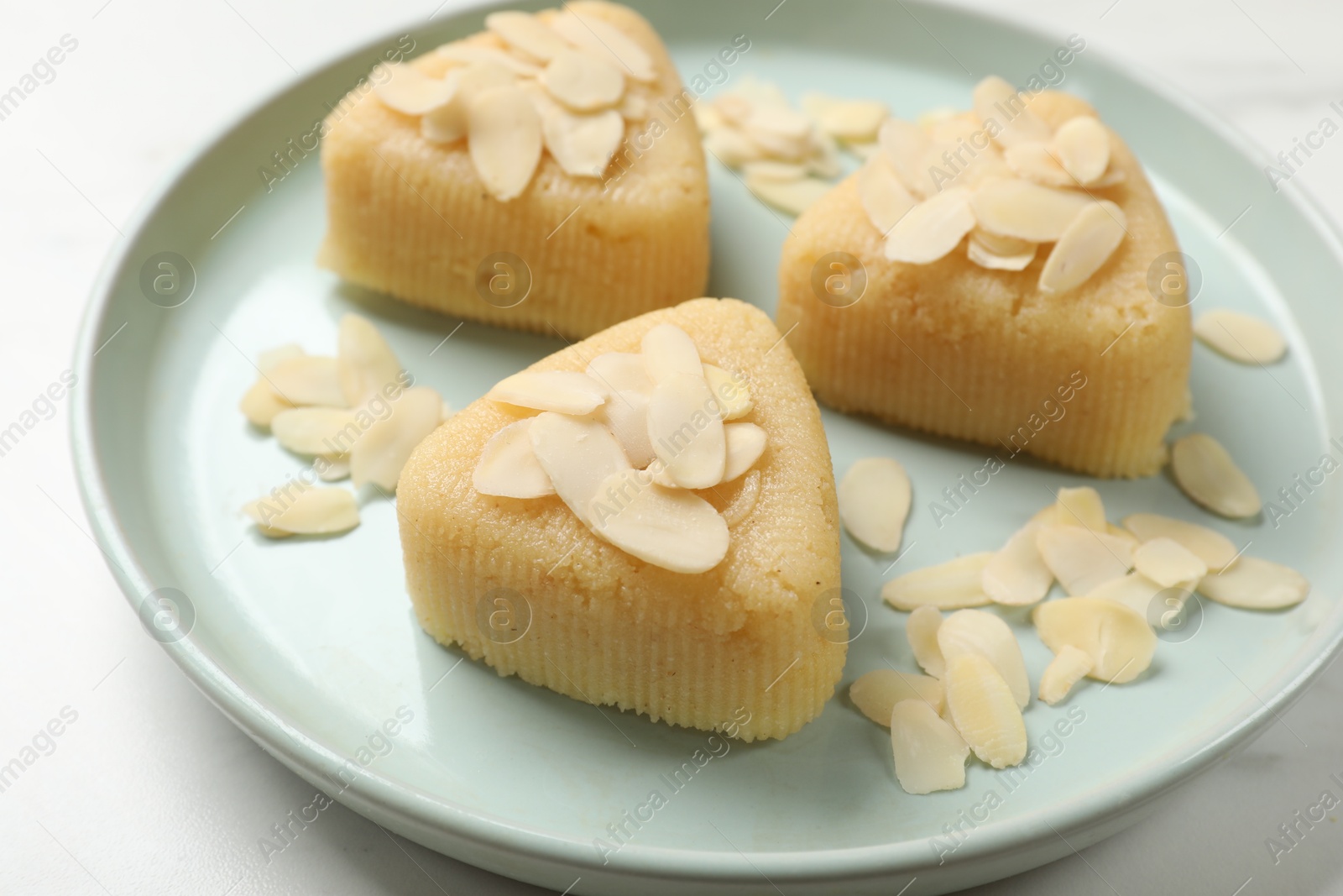 Photo of Pieces of delicious semolina halva with almond flakes on white table, closeup