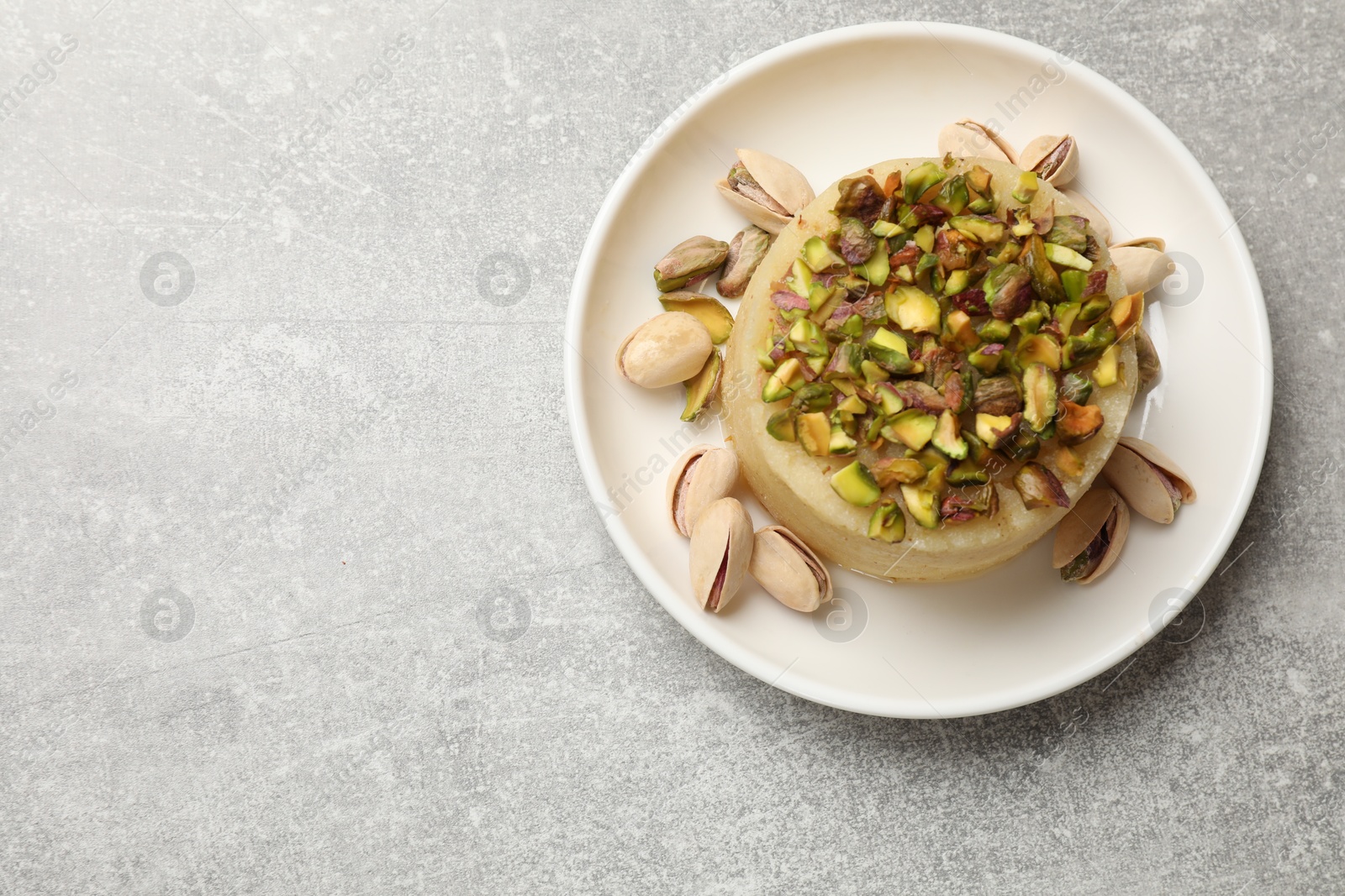 Photo of Delicious sweet semolina halva with pistachios on light grey table, top view. Space for text