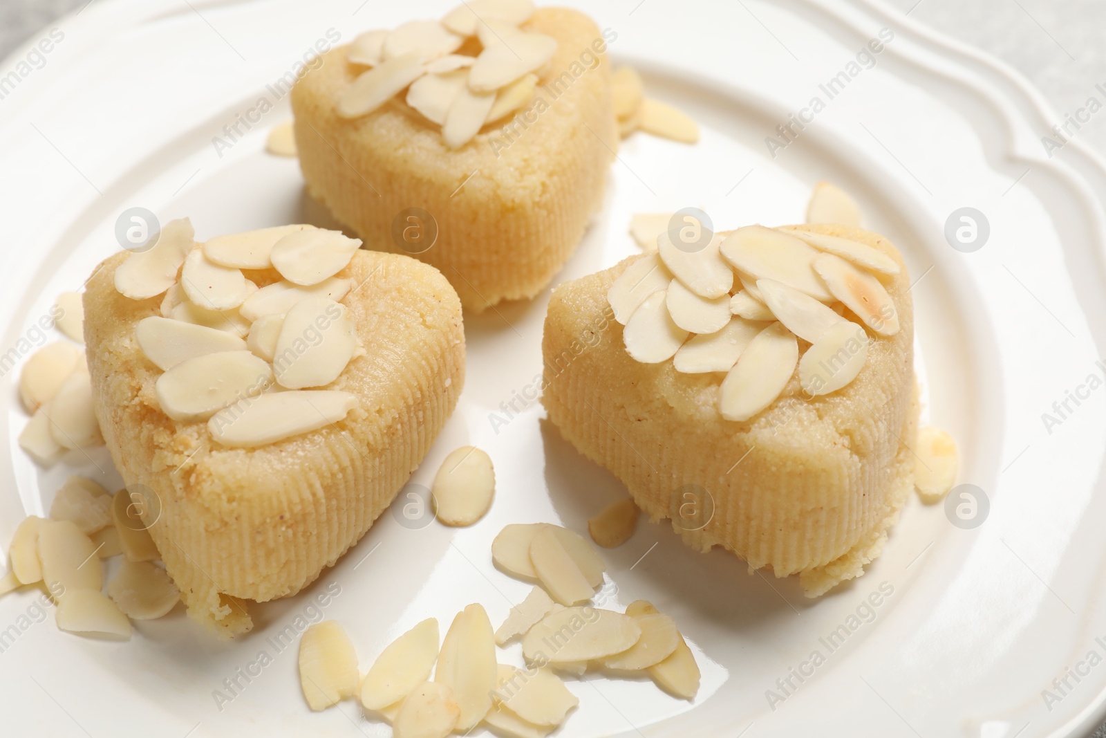 Photo of Pieces of delicious sweet semolina halva with almond flakes on plate, closeup