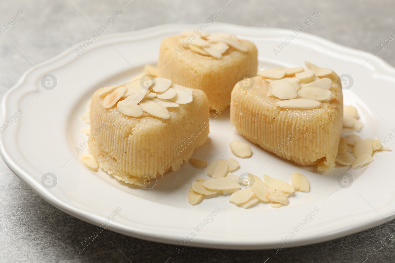 Photo of Pieces of delicious sweet semolina halva with almond flakes on light grey table, closeup