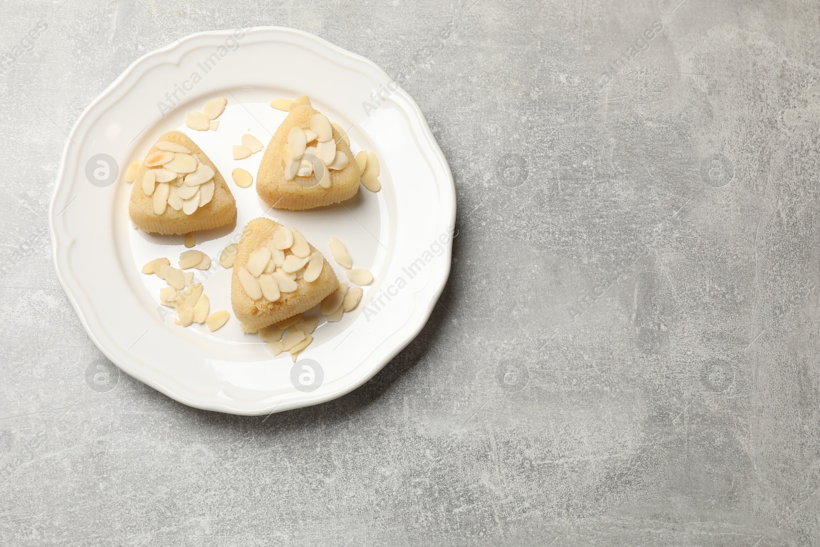 Photo of Pieces of delicious sweet semolina halva with almond flakes on light grey table, top view. Space for text