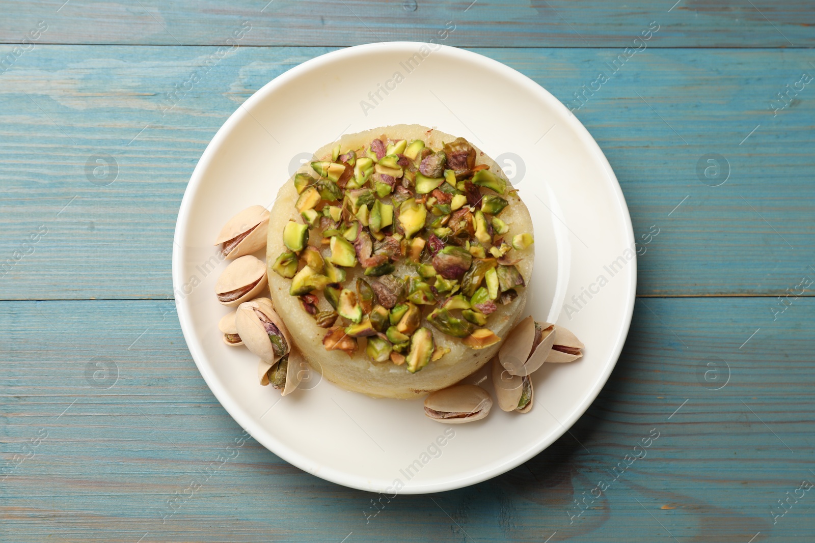 Photo of Delicious sweet semolina halva with pistachios on blue wooden table, top view