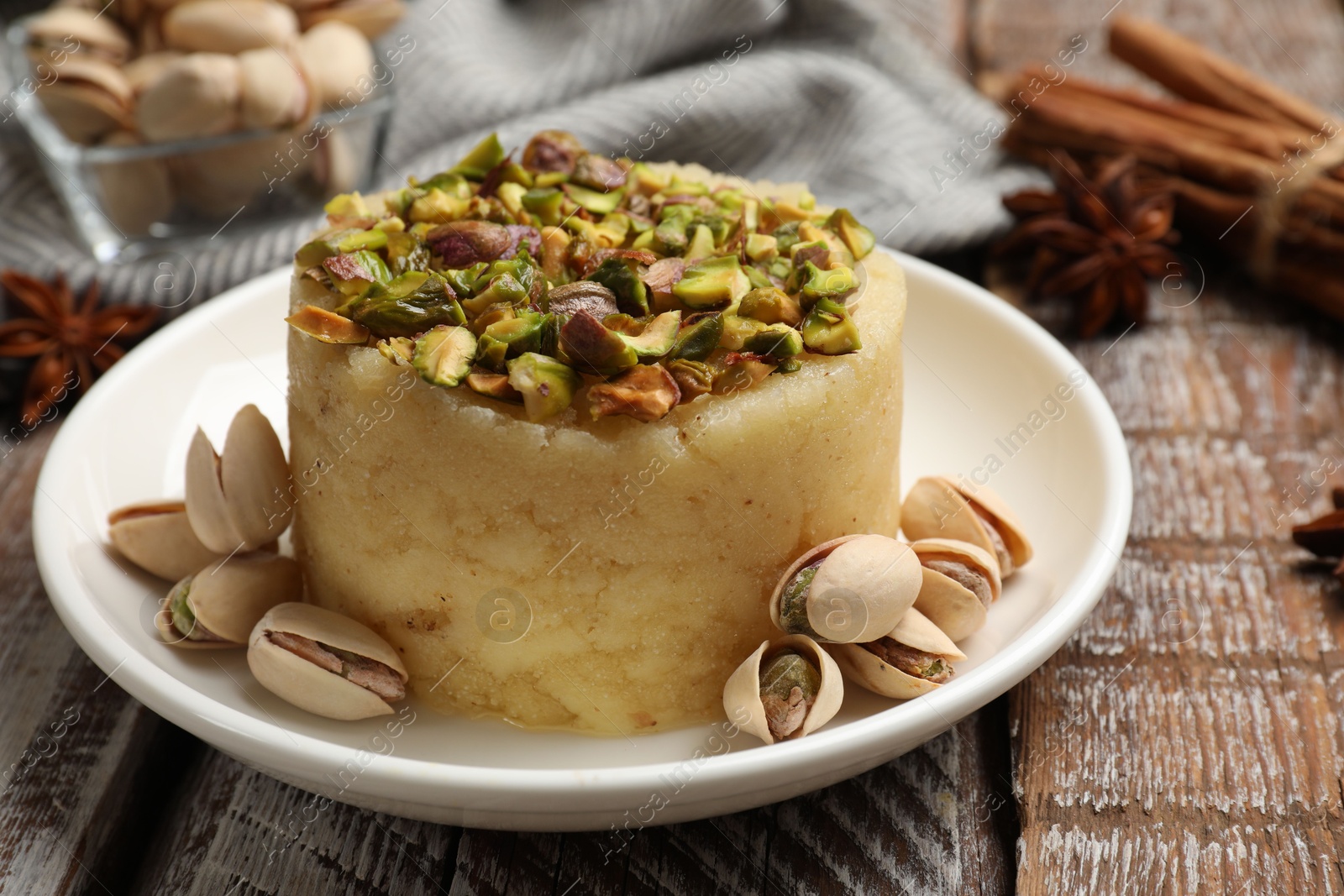 Photo of Delicious sweet semolina halva with pistachios and spices on wooden table, closeup