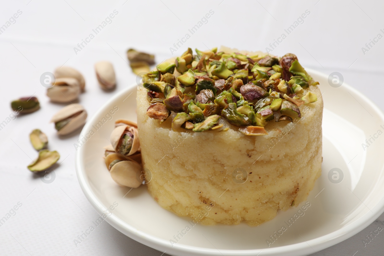 Photo of Delicious sweet semolina halva with pistachios on white tiled table, closeup