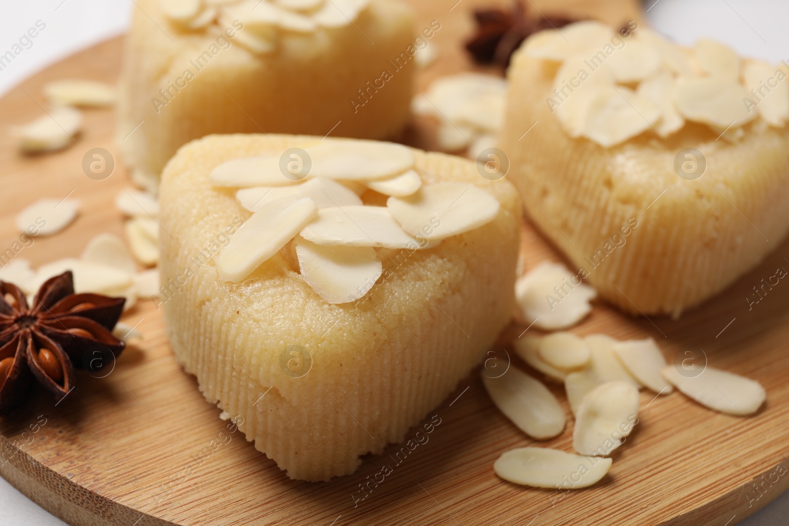 Photo of Pieces of delicious sweet semolina halva with almond flakes on wooden board, closeup