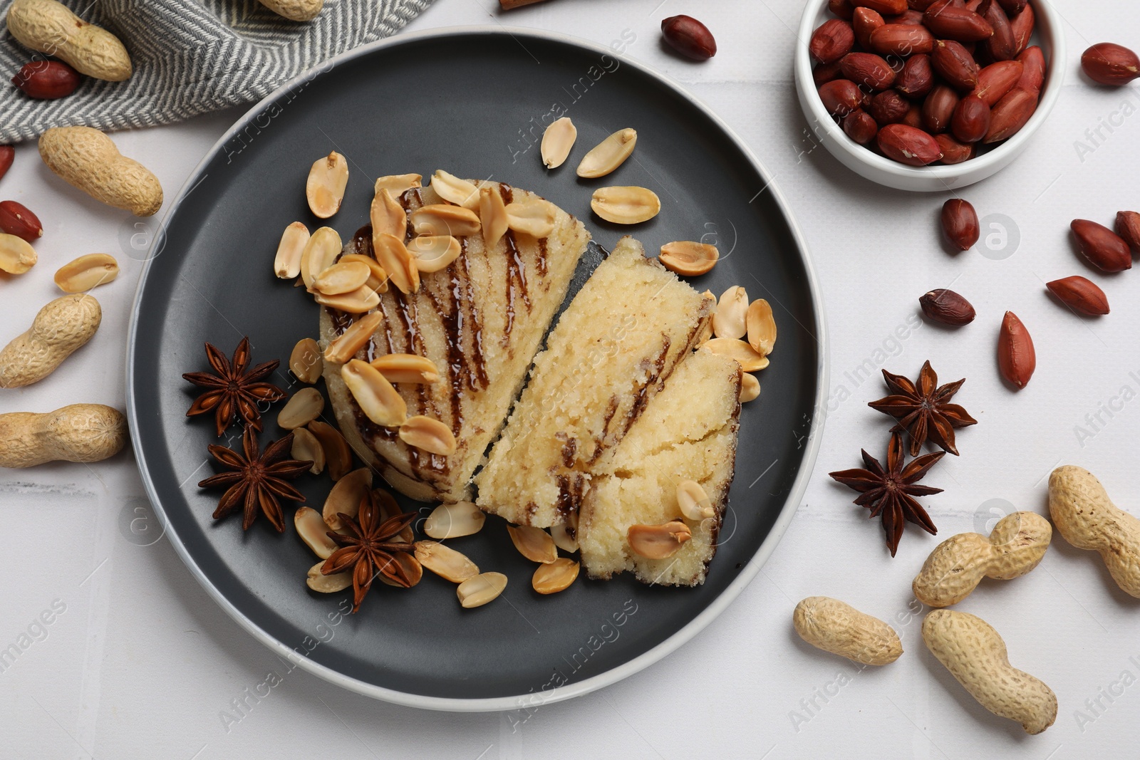 Photo of Delicious sweet semolina halva with peanuts and spices on white tiled table, flat lay