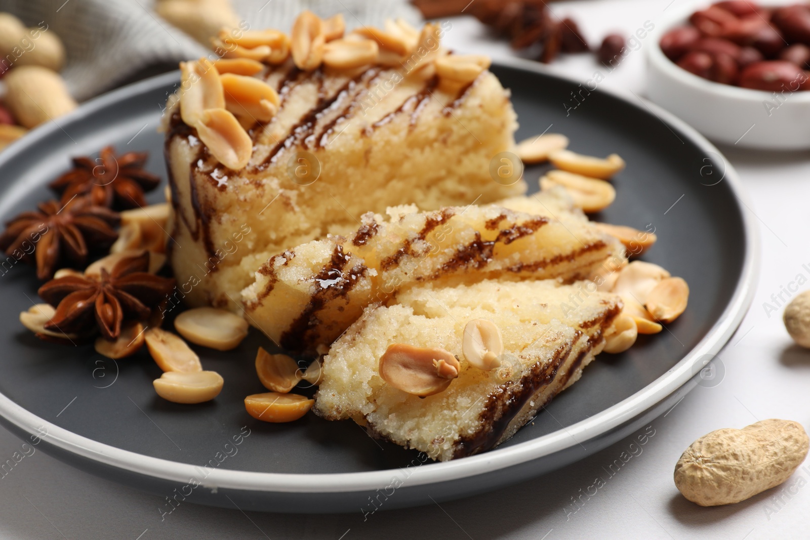 Photo of Delicious sweet semolina halva with peanuts and spices on white table, closeup