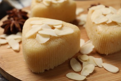 Photo of Pieces of delicious sweet semolina halva with almond flakes on wooden board, closeup