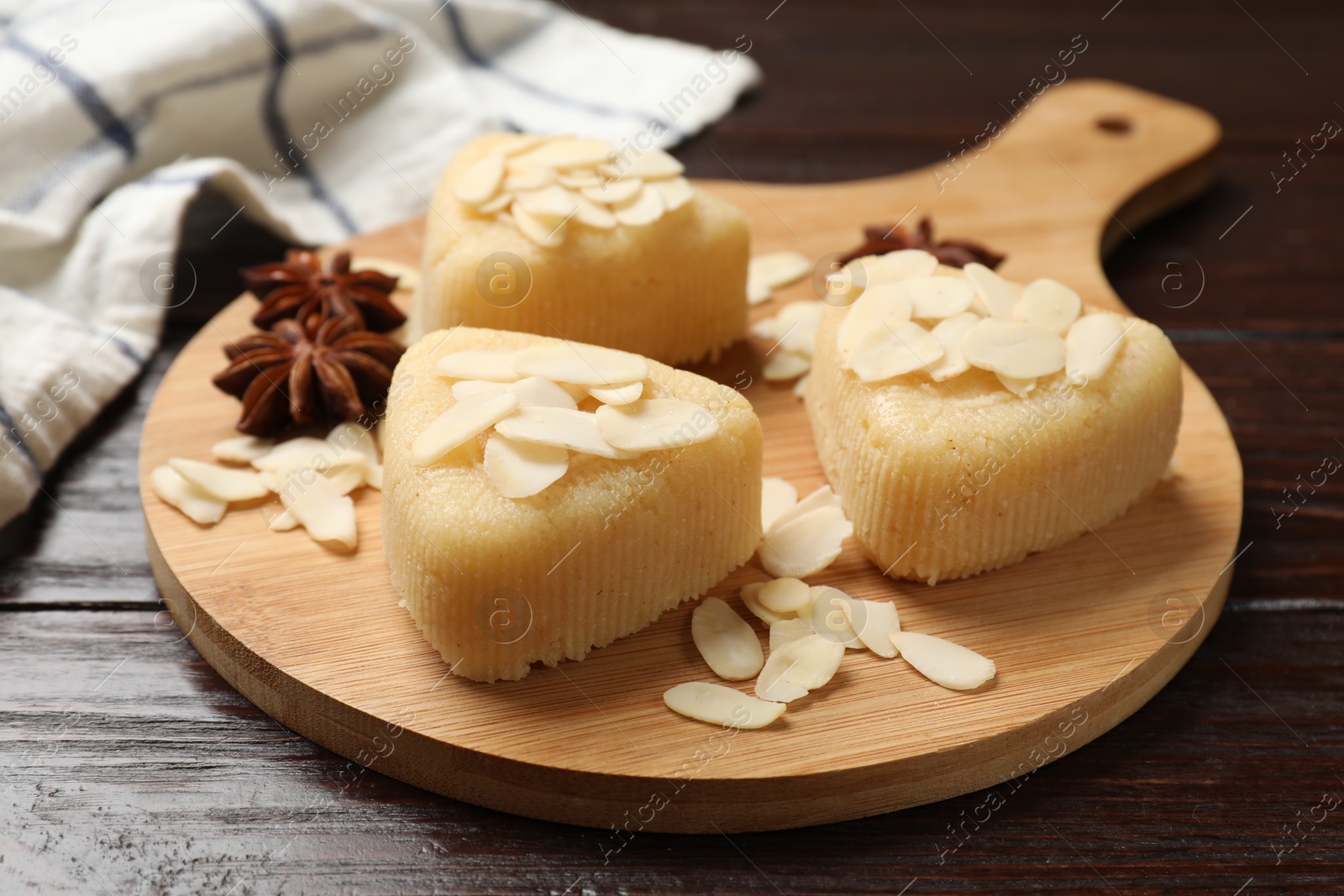 Photo of Pieces of delicious sweet semolina halva with almond flakes on wooden table, closeup