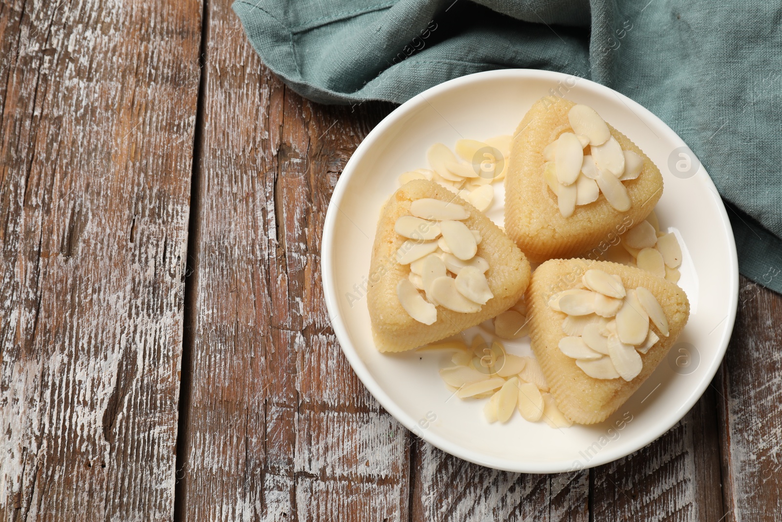 Photo of Pieces of delicious sweet semolina halva with almond flakes on wooden table, top view. Space for text