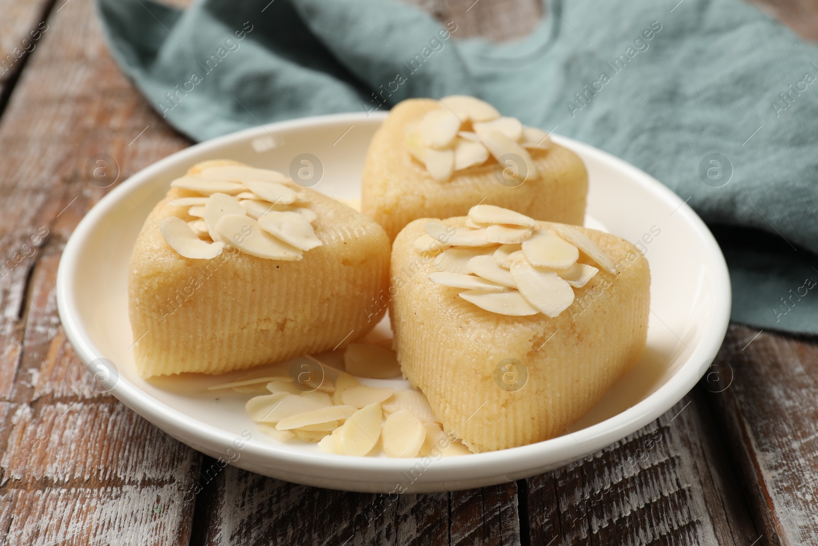 Photo of Pieces of delicious sweet semolina halva with almond flakes on wooden table, closeup