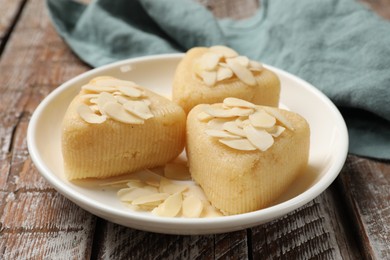 Photo of Pieces of delicious sweet semolina halva with almond flakes on wooden table, closeup