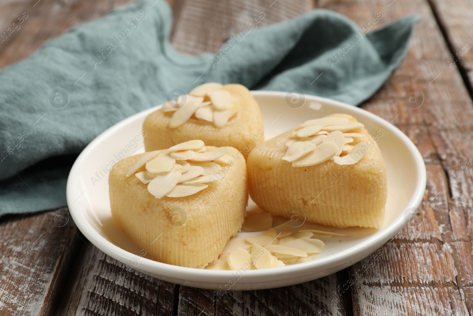 Photo of Pieces of delicious sweet semolina halva with almond flakes on wooden table, closeup