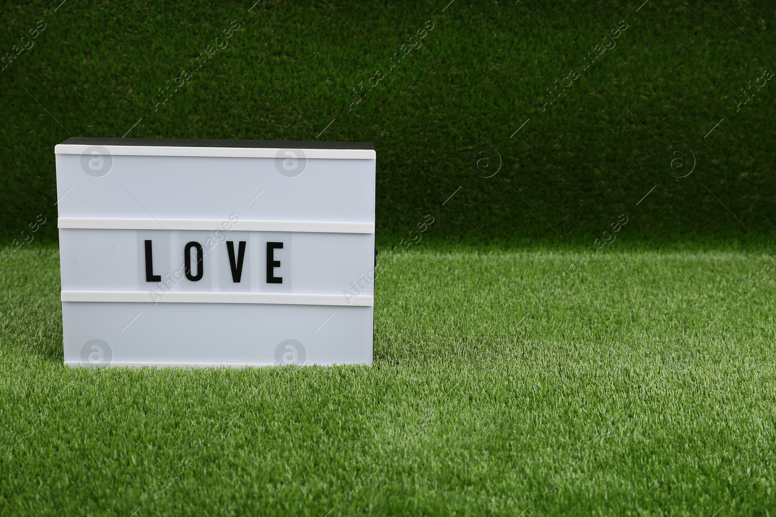 Photo of Lightbox with word Love on green grass. Space for text