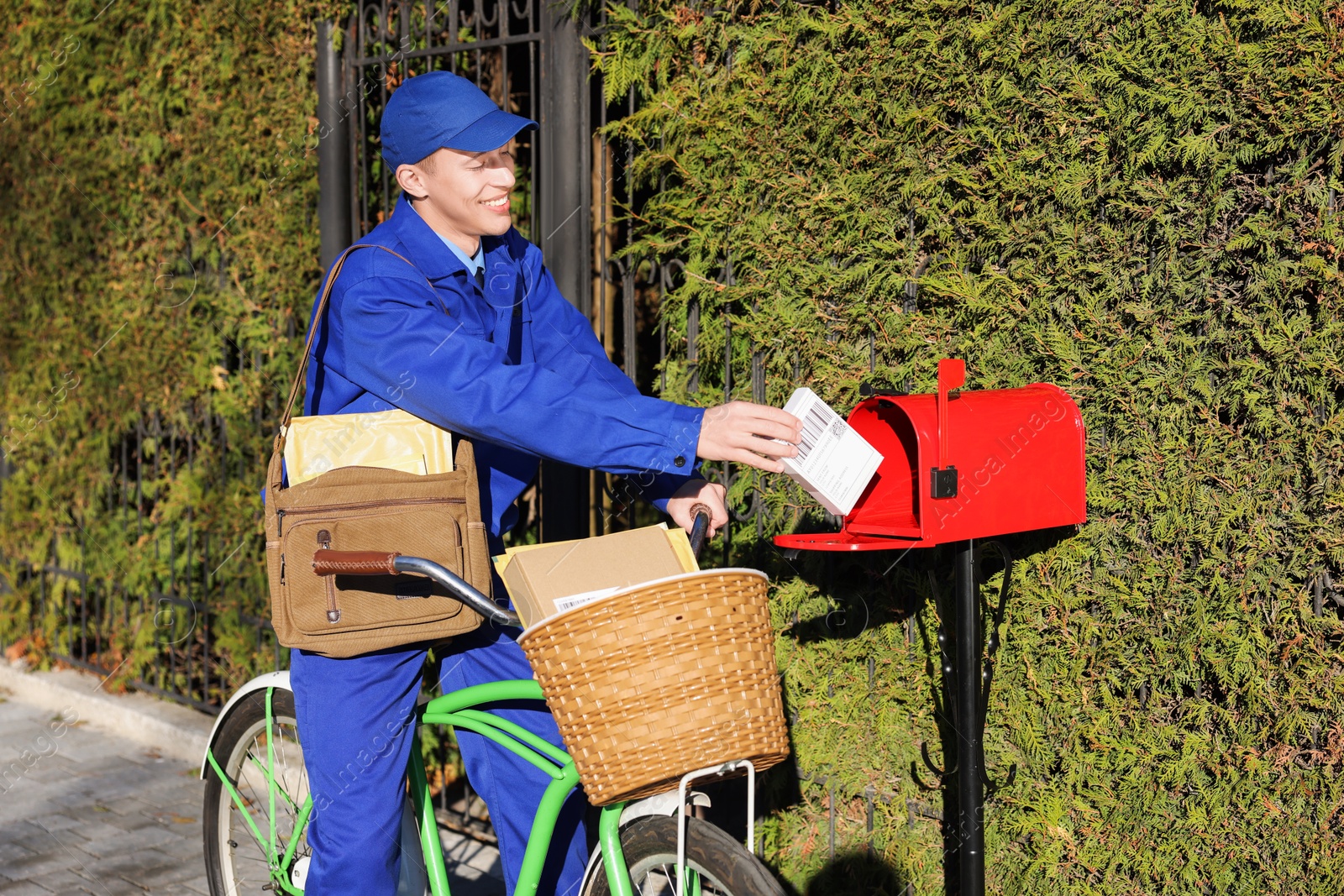 Photo of Postman with bicycle putting parcel into mail box outdoors