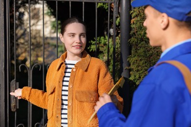 Photo of Woman receiving parcel from postman outdoors. Mail service