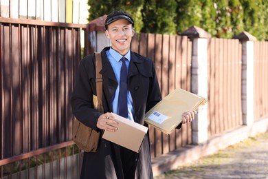 Happy postman with parcels outdoors. Mail service