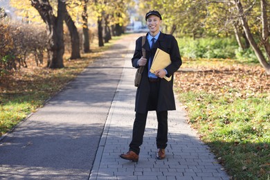 Photo of Happy postman with bag and envelopes outdoors