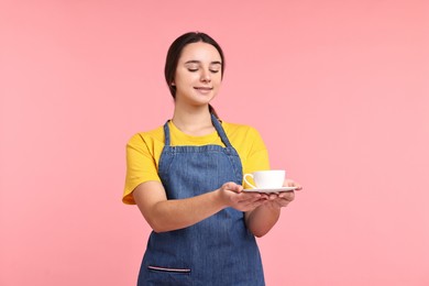 Photo of Girl in apron with cup of coffee on pink background. Work for teenagers