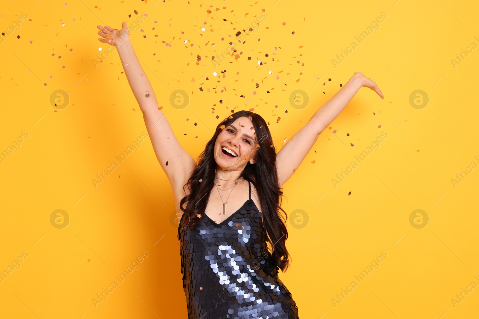 Photo of Happy woman under falling confetti on orange background. Surprise party