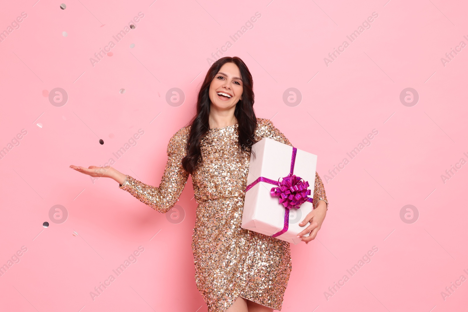 Photo of Happy woman with gift box and flying confetti on pink background. Surprise party