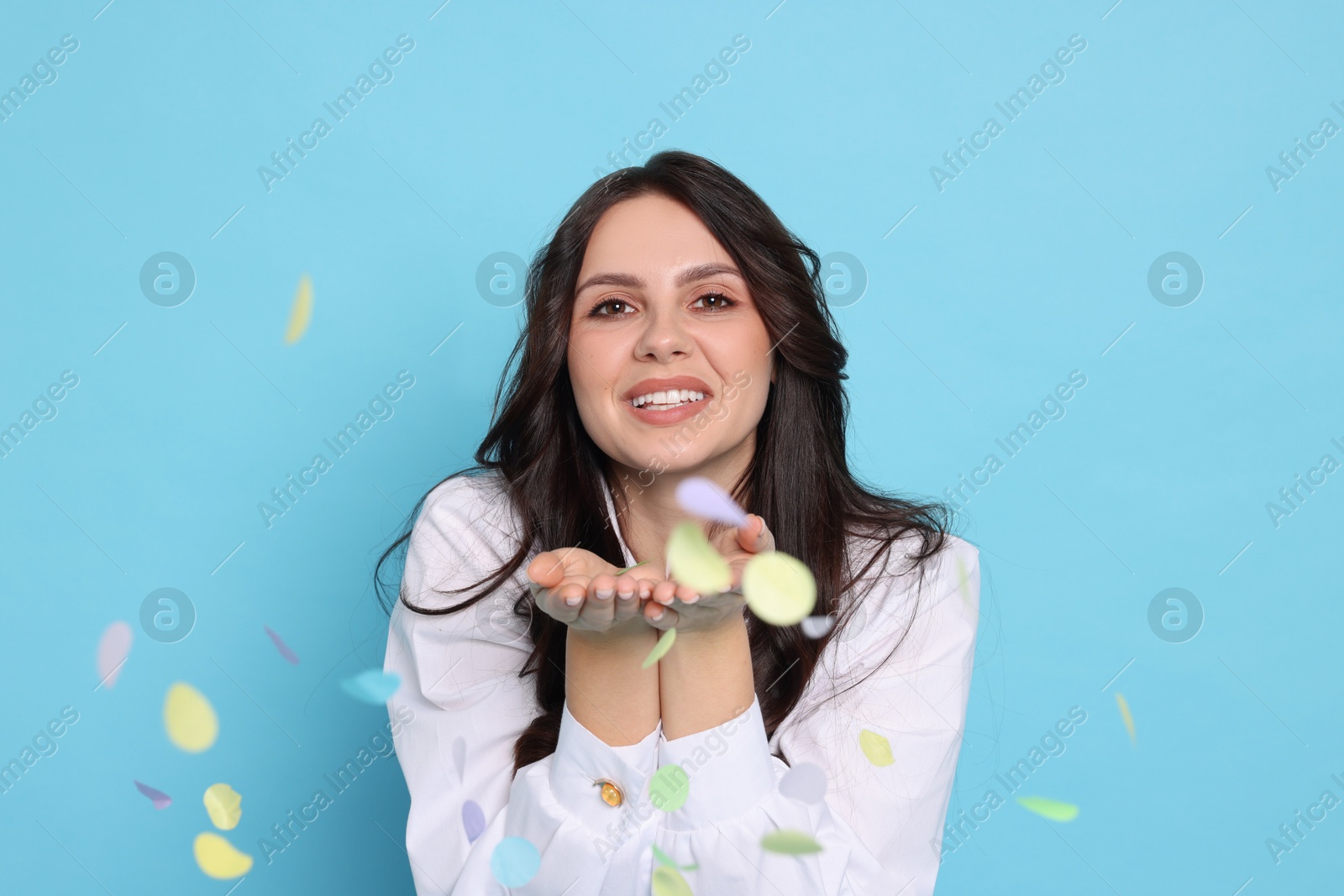 Photo of Happy woman with confetti on light blue background. Surprise party