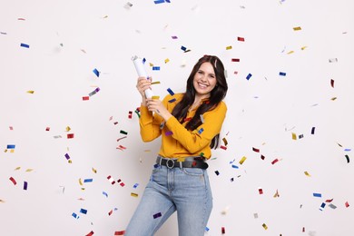 Photo of Happy woman blowing up confetti popper on white background. Surprise party