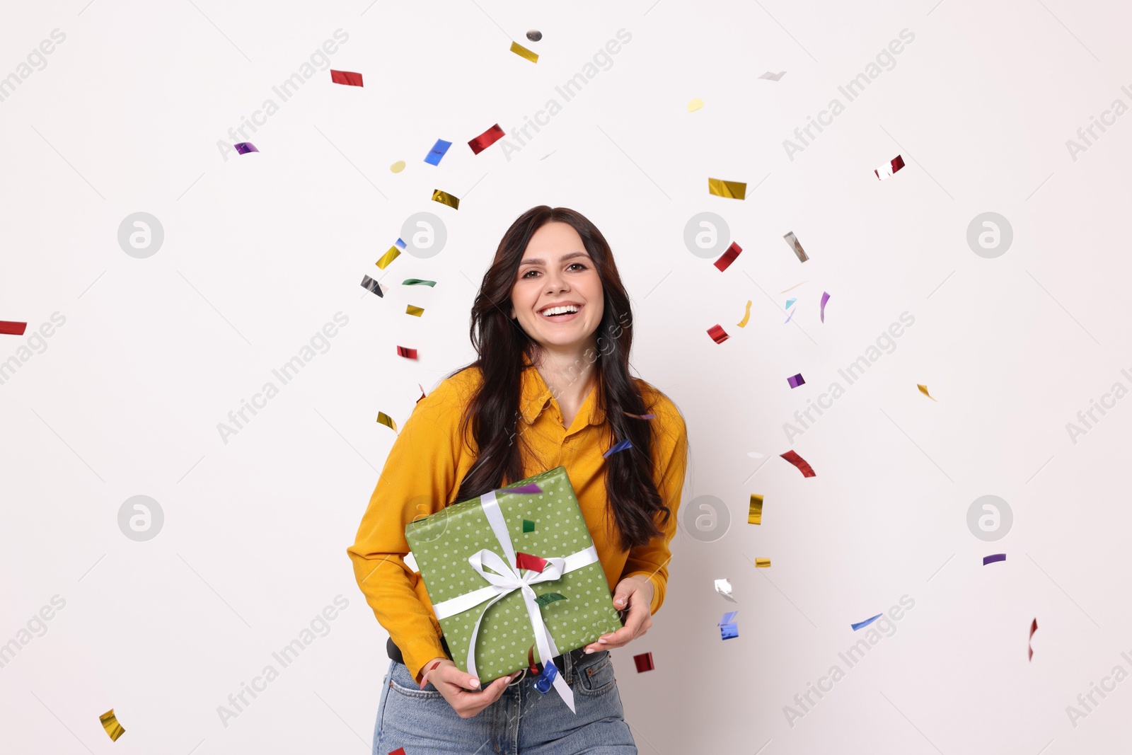 Photo of Happy woman with gift box and falling confetti on white background. Surprise party