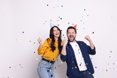 Happy friends in conical paper hats having fun under falling confetti on white background. Surprise party