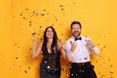 Happy friends having fun under flying confetti on orange background. Surprise party