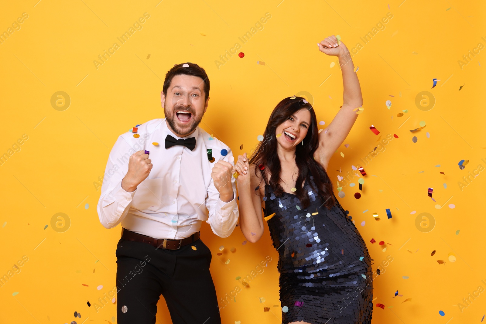 Photo of Happy friends having fun under flying confetti on orange background. Surprise party