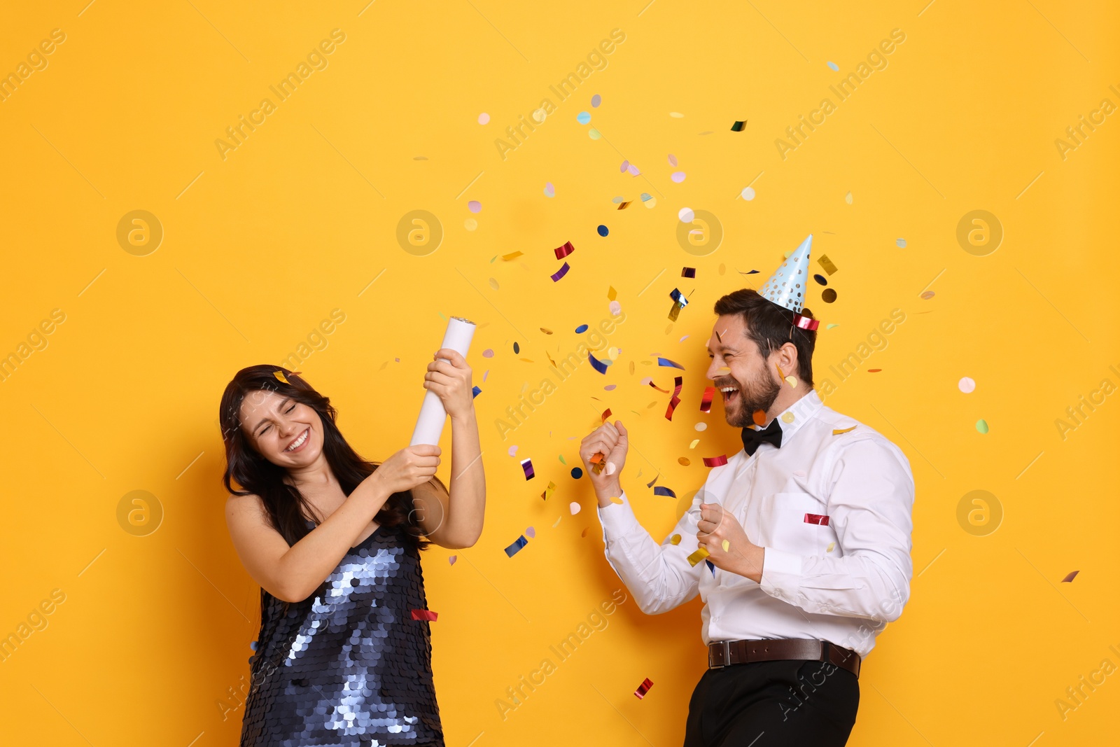 Photo of Happy friends blowing up confetti popper on orange background. Surprise party