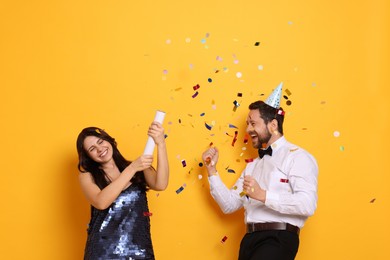 Photo of Happy friends blowing up confetti popper on orange background. Surprise party