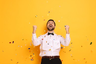 Photo of Happy man and flying confetti on orange background. Surprise party