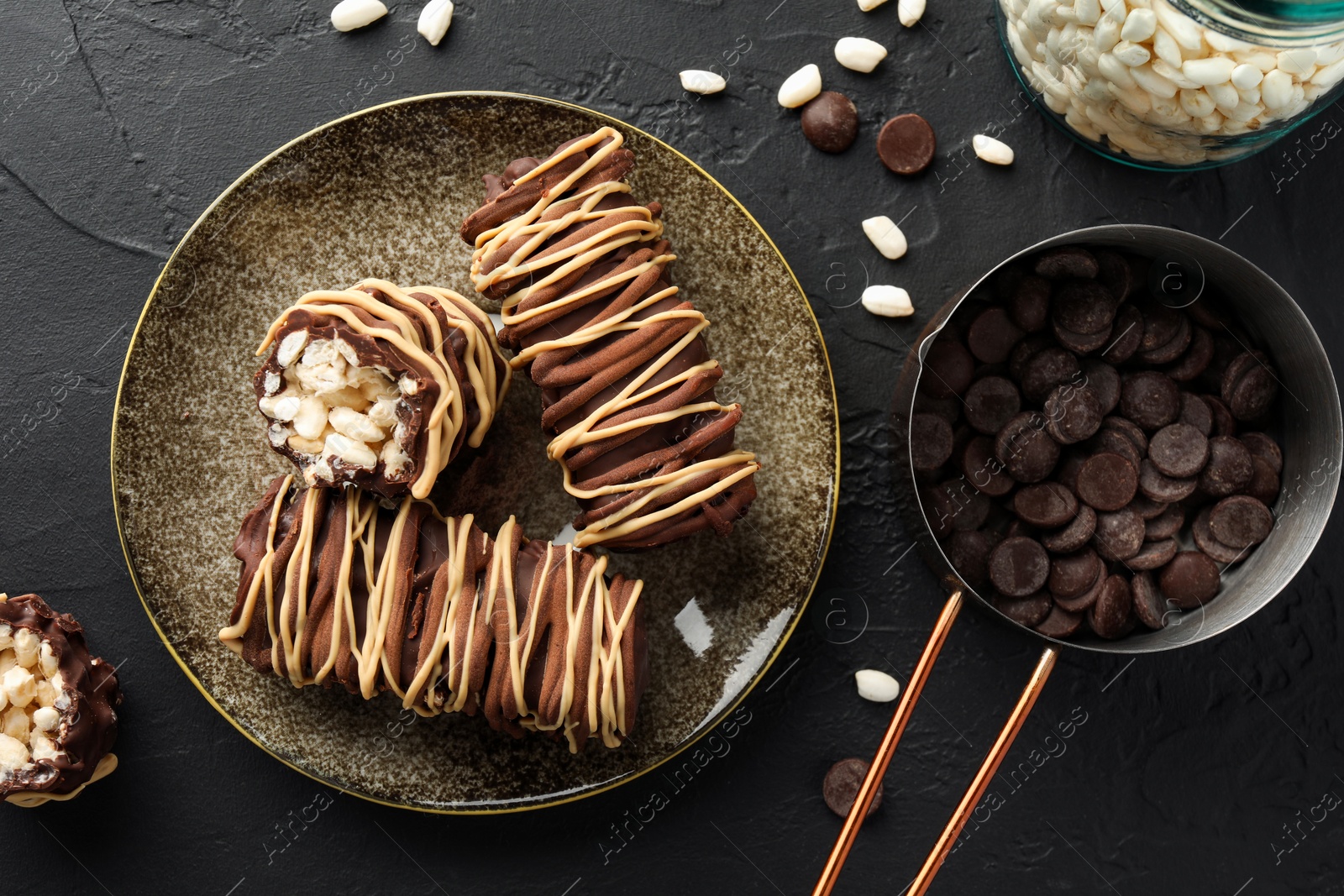 Photo of Delicious chocolate puffed rice bars and ingredients on dark gray textured table, flat lay