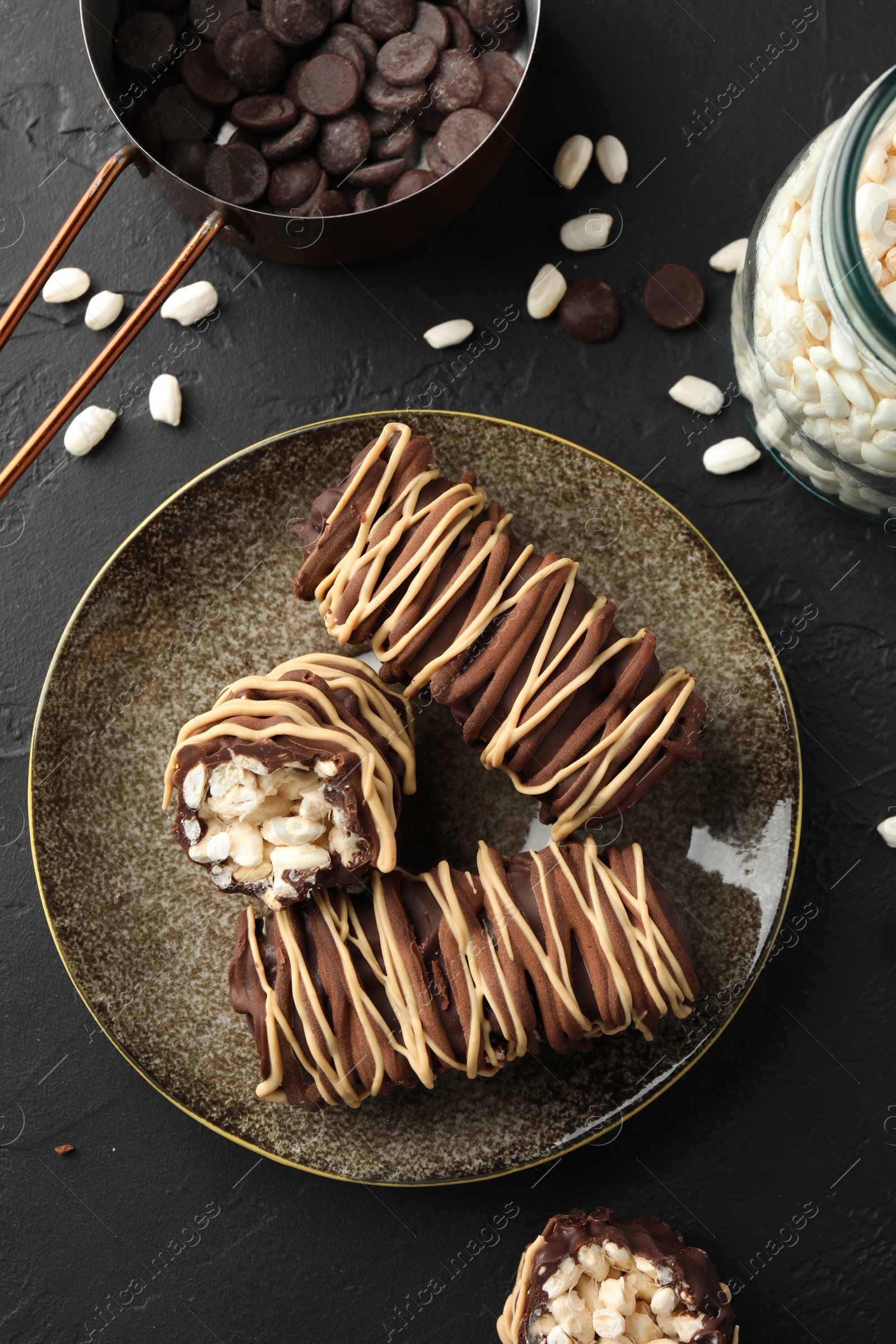 Photo of Delicious chocolate puffed rice bars and ingredients on dark gray textured table, flat lay