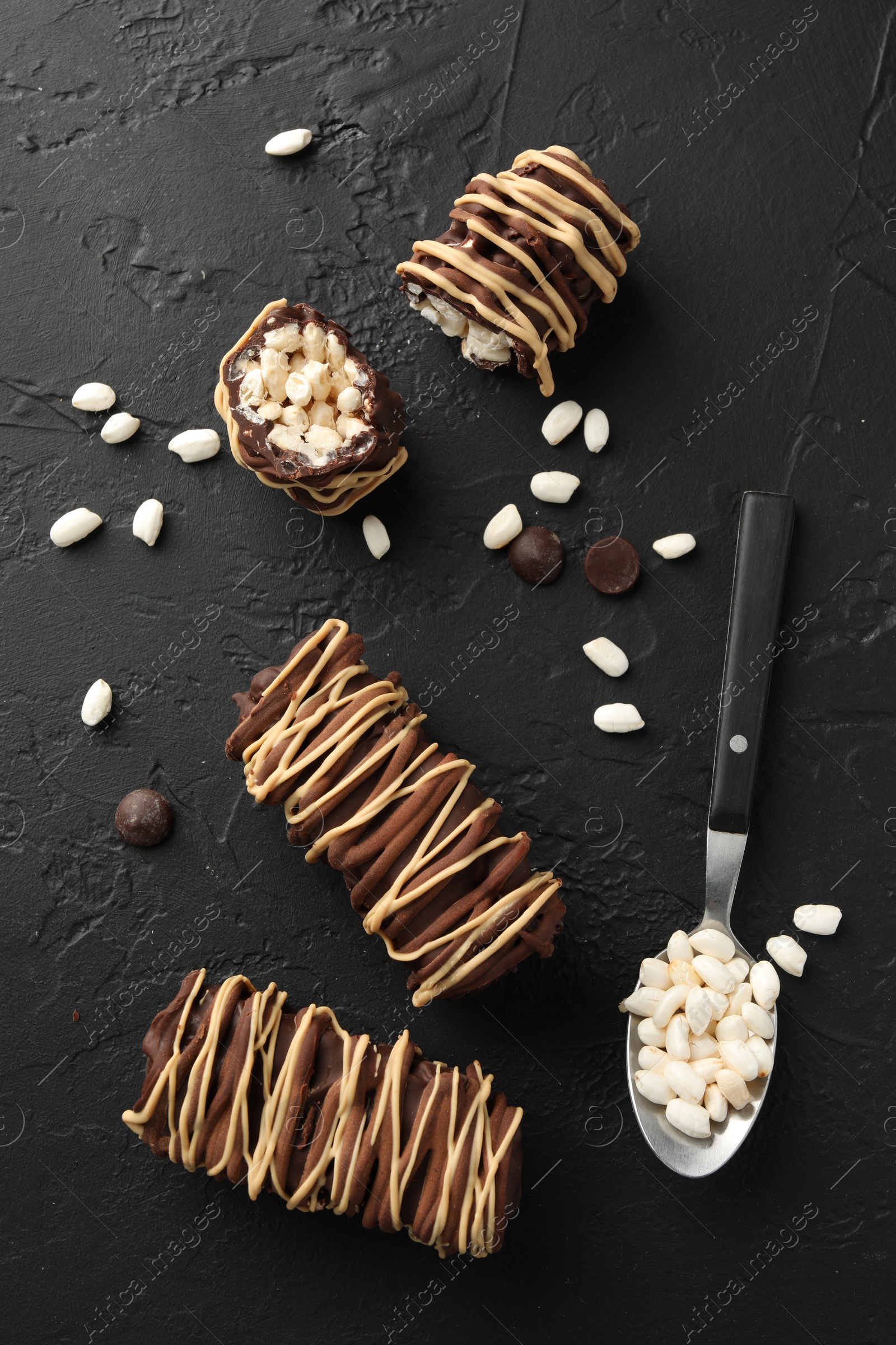 Photo of Delicious chocolate puffed rice bars and spoon on dark gray textured table, flat lay